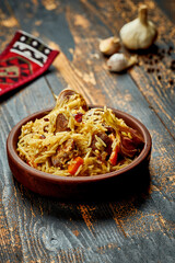 Classic pilaf with beef, garlic and carrots in a clay plate on a wooden background. Rustic