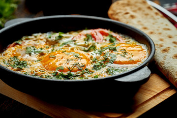 Fried eggs with tomatoes, onions and pita bread in a pan on a wooden background. Tasty Shakshuka