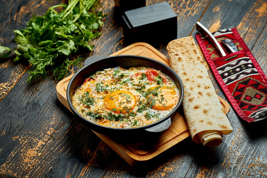 Fried eggs with tomatoes, onions and pita bread in a pan on a wooden background. Tasty Shakshuka