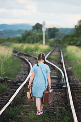 A little girl in a dress walking on an abandoned railroad tracks