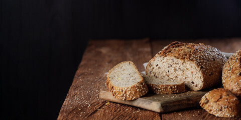 Rustic whole grain bread on a cutting board on a wooden kitchen table. Panorama, black background...