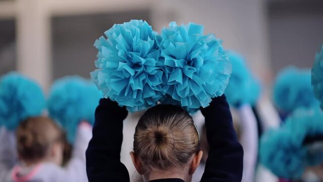Young cheerleader holding blue cheerleading pom-poms