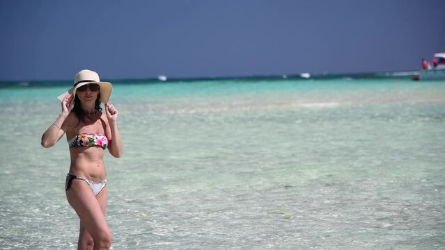 Woman wearing straw hat enjoying crystal clear waters ocean, slow motion