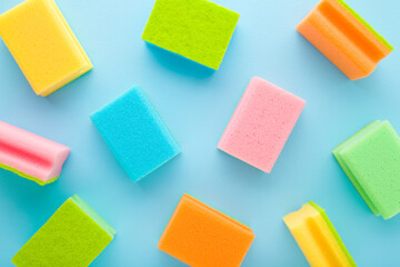 New colorful dry sponges on light blue table background. Pastel color. Closeup. Pattern of cleaning products. Top down view. - obrazy, fototapety, plakaty