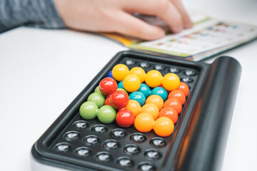 Close up board game with black field and colorful balls in holes against blurred hand with game rules. Solve riddle and find solution in puzzle. Connect, make shape IQ and intellectual activity