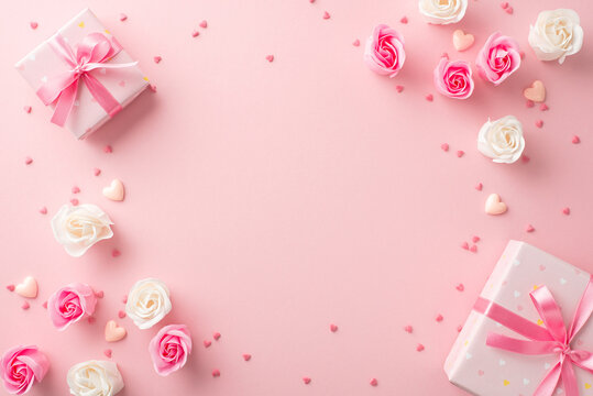 Mother's Day decorations concept. Top view photo of stylish gift boxes with ribbon bows white and pink roses small hearts and sprinkles on isolated pastel pink background with copyspace in the middle