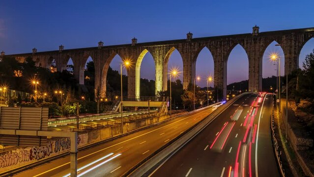 Time-lapse of highway traffic near Campolide station with Aguas Livres Aqueduct in background in the evening with car lights trails. Lisbon, Portugal. Zoom out effect