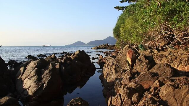 Scenic view of the calm horizon with a boat sailing by off the rocky coast of Rabbit Island or Koh Tonsay, a popular summer travel destination in Cambodia