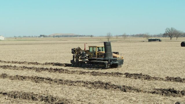 Industrial tile plow trench digger digging on a rural field, laying underground drainage pipe