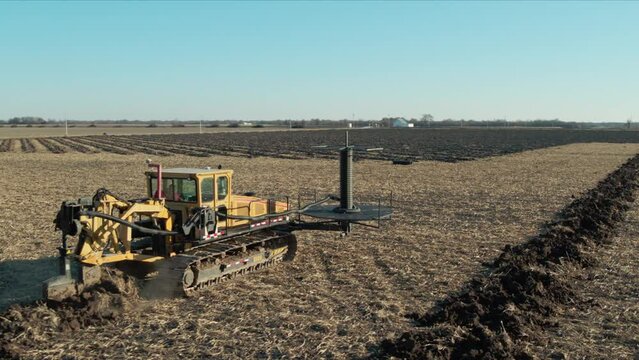 Aerial, tile plow digging line in a soil field installing drainage pipe underground
