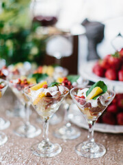 Decorated outdoor buffet. Dessert of berries and croutons with whipped cream in glass bowls. In the background are fruits and greens.