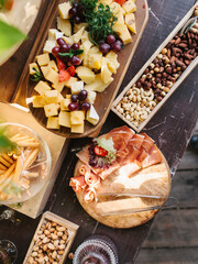 Decorated outdoor buffet. On a wooden table, cheese slices with fruits, prosciutto, jamon, cape, nuts, pistachios, bread sticks. Summer picnic, outdoor party.