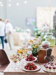 Decorated outdoor buffet. Fresh strawberries, fruit dessert in bowls, jelly, creamy desserts. The table is decorated with flowers, green leaves and branches.
