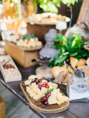 Decorated outdoor buffet. On a wooden table, cheese slices with fruits. Nuts, masinas, decorative sculptures and flowers are in the background. banquet decor, wedding, picnic.