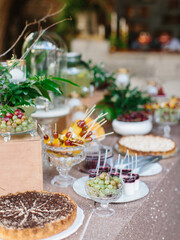 Decorated outdoor buffet. In the foreground is a pie, vases with berries and fruit slices. In the background are greens, appetizers and desserts.