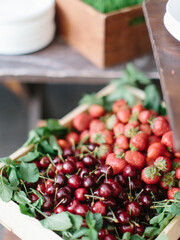 Fresh ripe cherries and strawberries lie with mint leaves in a wooden box.