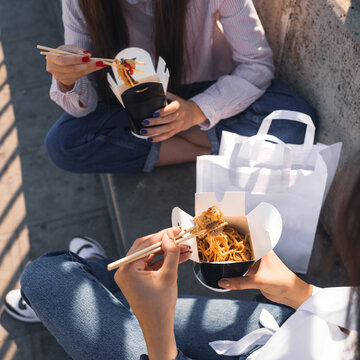 Young woman eating Wok Noodles asian food using choopsticks from take away delivery