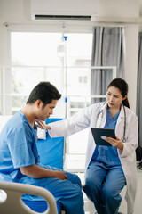 Asian doctor in white suit take notes while discussing and Asian elderly, man patient who lying on bed with receiving saline solution in hospital. .