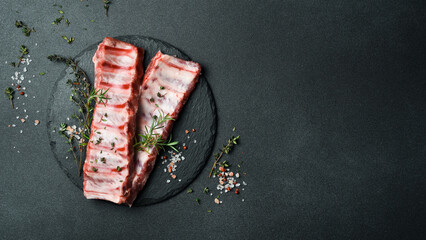 Fresh raw ribs with rosemary, spices and herbs. On a dark slate background. Top view. Free space for text.