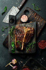 grilled medium-rare beef steak on a T-bone on a wooden board with rosemary. On a dark slate background.