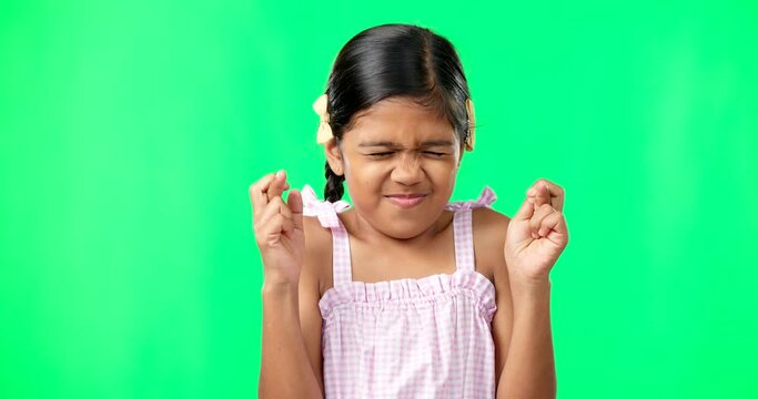 Child, wish and fingers crossed on green screen for luck or faith. Girl kid or eyes closed emoji for hope, praying and miracle or help on studio background space with mockup space while hopeful