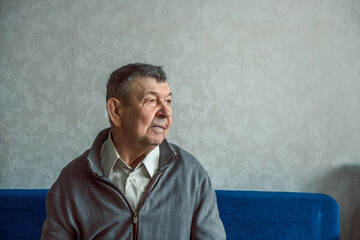Portrait of sad elderly man on grey background. Thoughtful look of old senior sitting alone at...