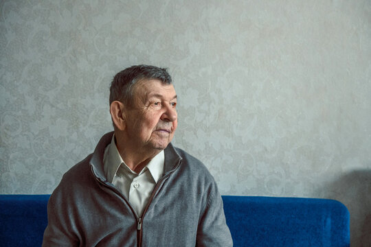 Portrait Of Sad Elderly Man On Grey Background. Thoughtful Look Of Old Senior Sitting Alone At Home. Close-up Of Wrinkled Face, Copy Space. High Quality Photo