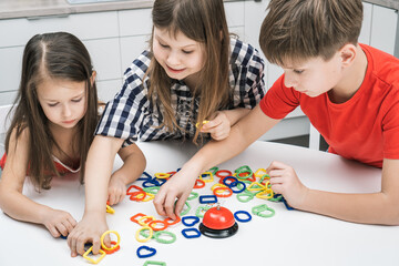 Smiling, pensive children of boy and girls connecting colorful chain figures, solve and make puzzle constructor of heart, triangle, square for time. Strategic and logical game for kids development