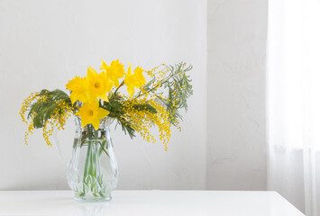 yellow spring flowers in glass vase on white background
