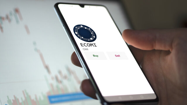 March 11 2023 London UK. An investor's analyzing the ECOMI  coin on screen. A phone shows the crypto's prices to invest in OMI