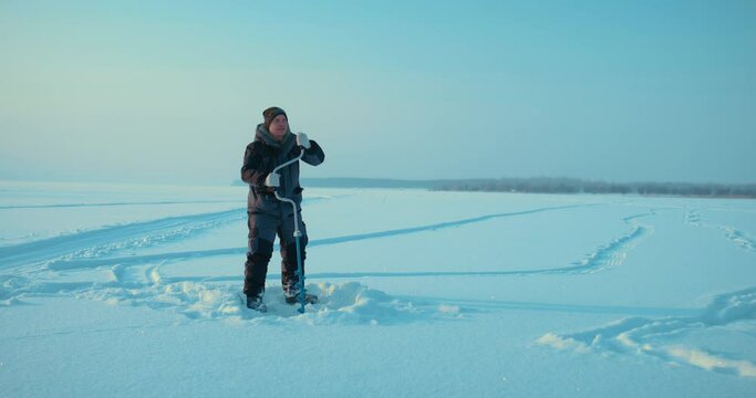 experienced ice fisher drilling ice for catching fish in winter, full-length portrait, 4K, Prores