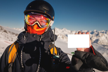 snowboarder holds an empty lift pass with a mountain in the background. Blank ski pass in the hand...