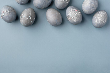 Festive Easter background. Gray-blue Easter eggs with stars on a blue table. Banner with a place for text. Top view.