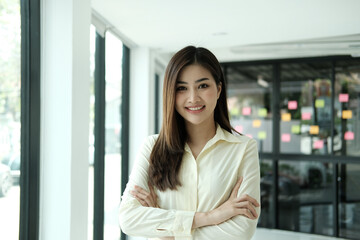Young confident smiling Asian business woman leader, successful entrepreneur, elegant professional company executive ceo manager, wearing suit standing in office with arms crossed. Portrait