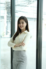Smiling young Asian business woman manager wearing suit holding notebook standing in modern glass office. Professional executive manager, corporate leader looking at camera. Portrait