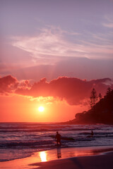 Surfer heading in to the ocean at Burleigh beach with with orange sunrise skies, Gold Coast Australia
