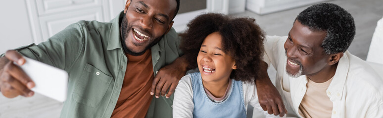 cheerful african american man taking selfie on smartphone with happy daughter and father, banner.