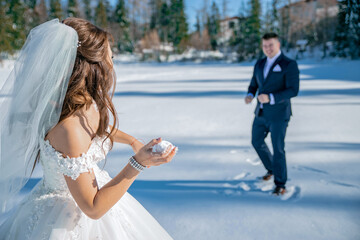 Young couple bride and groom playing in the winter nautre under snowy mountains on a frozen lake. playing snowball fight. throwing snow balls on each other. having a great time. laughing