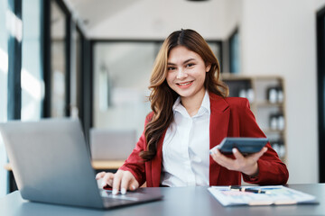 Beautiful young teen asian businesswoman using computer laptop and calculator for calculate with planning working on financial document, tax, exchange, accounting and Financial advisor