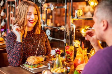 Beautifull nice couple wife and husband enjoying their burger. Hamburger eating in restaurant. Playing with food. Industrial style restaurtant. Restart burger. Mcdonalds. Date in restaurant.