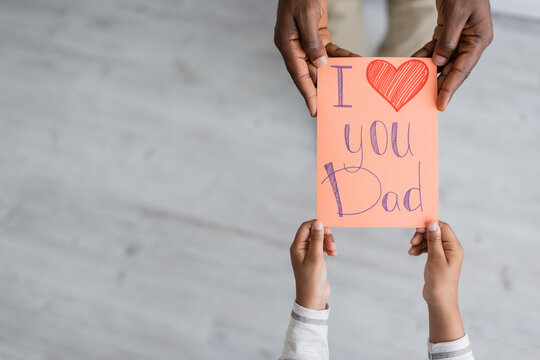 top view of cropped african american child holding greeting card with i love you dad lettering near man on fathers day.