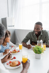 happy african american girl looking at cheerful father while having family breakfast.