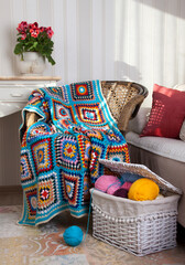 Bright beautiful hand-knitted plaid on a wicker chair and a basket with colored yarn