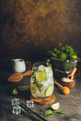 Iced Mojito cocktail long rum drink with fresh mint, fresh thyme, lime juice, cane sugar and soda on dark abstract background. Summer iced beverage and cocktail