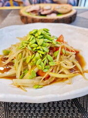 Green acacia seeds are sprinkled on papaya salad with crab and fermented fish to enhance the taste. Papaya salad with crab and pickled fish lime juice, chili,  yard long beans in a white plate 
