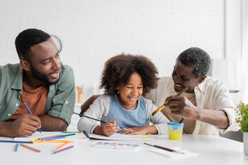 Cheerful african american parents painting with child at home.