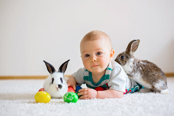 Little toddler child, baby boy, playing with bunnies and easter eggs at home