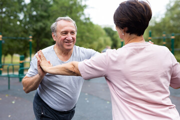Aged man and woman practicing gymnastics in open-air sports area