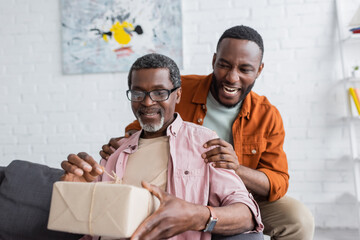 Smiling african american man hugging dad with gift during father day at home.