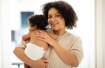 Happy loving young african american curly woman plus size holding baby in her arms in clinic or...
